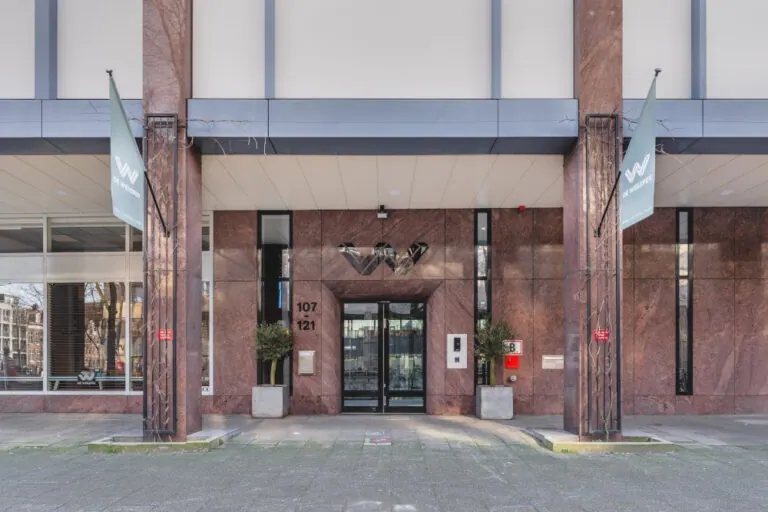 De entree van ons kantoor aan de Weesperstraat: een portiek van roodbruin marmer met twee vierkante zuilen, glazen deuren in zwarte kozijnen en de huisnummers 107 en 121 ernaast.